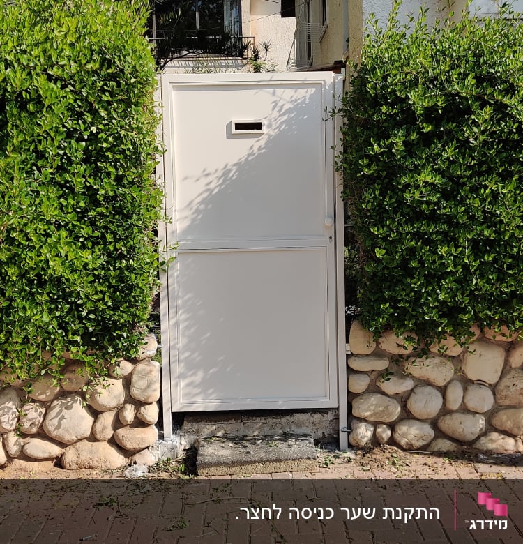 שער מתכת לבן בין שיחים ירוקים